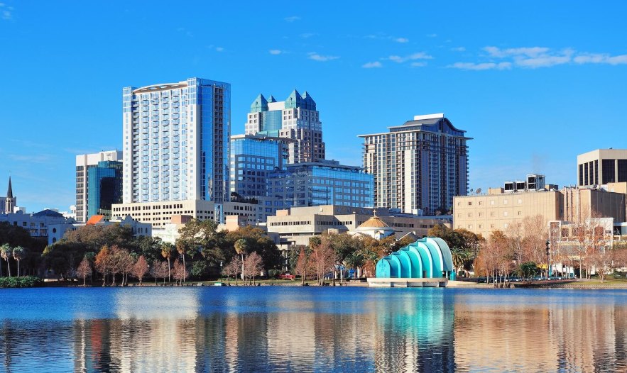 A city skyline reflected in a calm lake under a blue sky